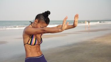 Bir kadın, tropik deniz sahilinde doğada yoga yapmakla meşgul.