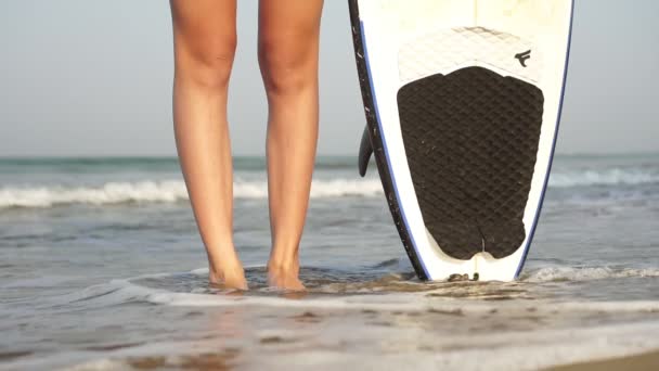 Młoda szczupła surferka w bikini z deską surfingową na tle morza — Wideo stockowe