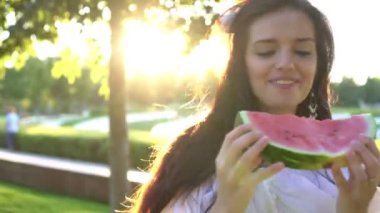 Genç ve güzel bir kadın bir yaz günü parkta olgun karpuz yiyor.