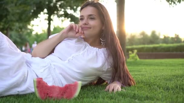 Piękna młoda kobieta leży w parku na zielonej trawie z kawałkiem arbuza — Wideo stockowe