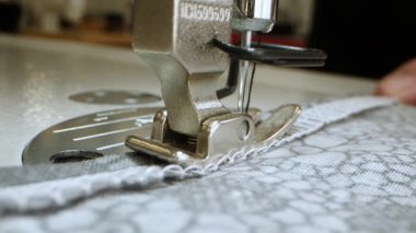 A womans hands hold a piece of cut fabric with a floral pattern, threading it under the needle of a sewing machine. The process of making clothes, close-up stitching