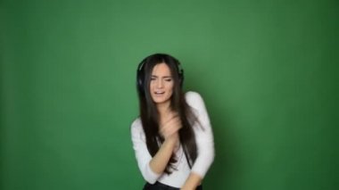 Kulaklık, müzik ve fuan konseptiyle dans eden güzel ve çekici bir kız. Şarkı söylüyor ve gülümsüyor yeşilde
