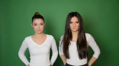 İki esmer beyaz kadın yeşil arka planda yalnız gülümsüyor.