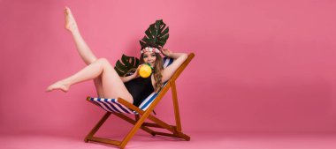 Plaj sandalyesinde gülümseyen kız, pembe arka planda izole edilmiş mayo giyiyor, mevsimlik yaz konsepti.