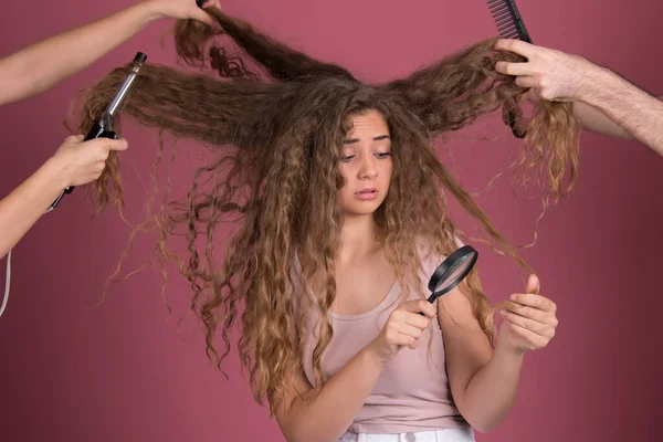Kuaför konsepti, uzun kıvırcık saçlı, elleri başının etrafında, elinde makas, tarak, demir, büyüteç olan güzel bir kadın.
