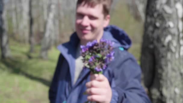 Boldog fiatalember ad a lány egy csokor a vadvirágok. Tavaszi parkban, a romantikus dátum. — Stock videók