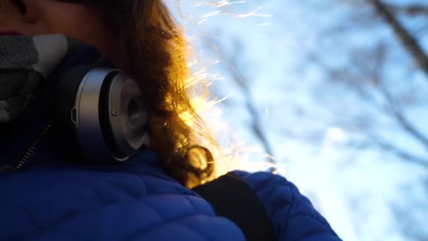 Una joven en el parque escuchando música con auriculares. Una mujer camina por el parque de primavera y disfruta de la música . — Vídeos de Stock