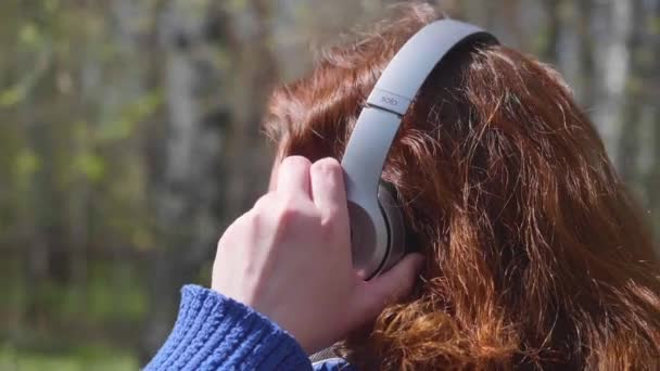一个女人参加体育运动 在耳机里欣赏音乐 公园里的一个年轻女孩戴着耳机听音乐 — 图库视频影像