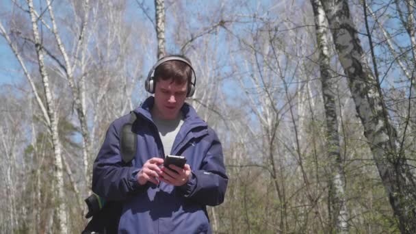 若い男は、ヘッドフォンを介して音楽を聴く、公園を散歩します。春の公園で新鮮な空気の朝の散歩. — ストック動画