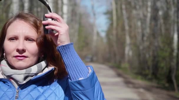 Una ragazzina al parco che ascolta musica con le cuffie. Una donna cammina attraverso il parco primaverile e godersi la musica . — Video Stock