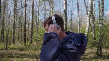 Genç bir adam bir parkta, kulaklık üzerinden müzik yapar. Sabah parkta temiz havada yürüyüş.