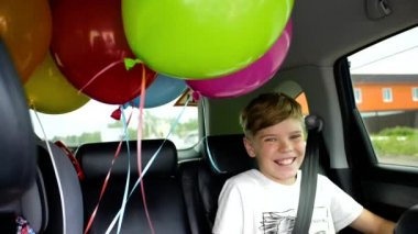 Mutlu bir çocuk bir arabaya binme. Şenlikli ruh hali, gülümseme, kahkaha. Arabada balonlar