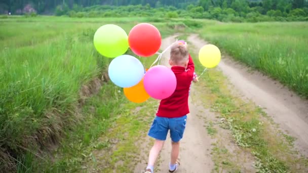 Crianças felizes correm em uma estrada florestal com balões. Celebração de aniversário no Parque. Risos e alegria das crianças — Vídeo de Stock