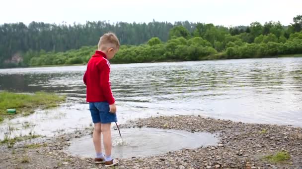 Un bambino che gioca sulle rive del fiume, il bellissimo paesaggio estivo. Attività ricreative all'aperto . — Video Stock