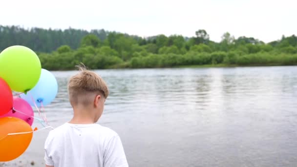 A teenager holds balloons. Summer holidays in nature near the lake. Celebration and fun.Childs birthday — Stock Video