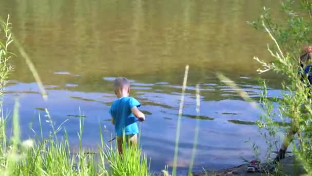 Dos niños atrapan peces con cañas de pescar en la orilla del río. Hermoso paisaje de verano. recreación al aire libre . — Vídeo de stock