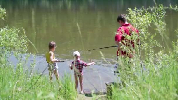 Dos niños pequeños y un joven padre pescando en la orilla del río. Hermoso paisaje de verano. recreación al aire libre . — Vídeos de Stock