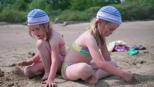 Deux filles jouent sur la plage faisant des figures de sable. Une chaude journée d'été. Vacances en famille au bord de la mer — Photo