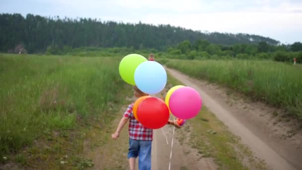 Niños felices corren por un camino forestal con globos. Celebración de cumpleaños en el Parque. Risa y alegría de los niños — Vídeos de Stock