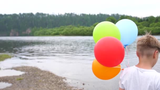 Un adolescente sostiene globos. Vacaciones de verano en la naturaleza cerca del lago. Celebración y divertido.Cumpleaños de niños — Vídeos de Stock