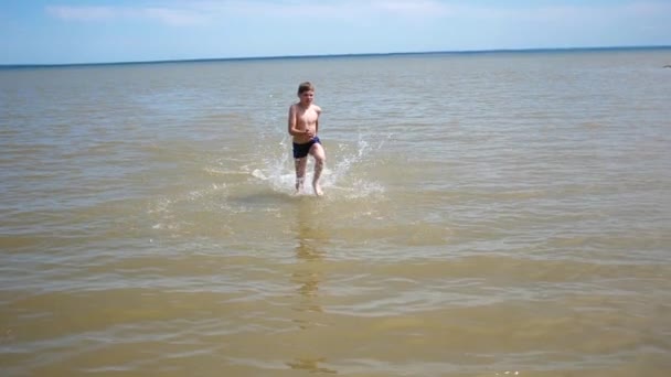 Niño feliz corre con placer en la playa. Aerosol de agua, día caluroso de verano — Vídeo de stock