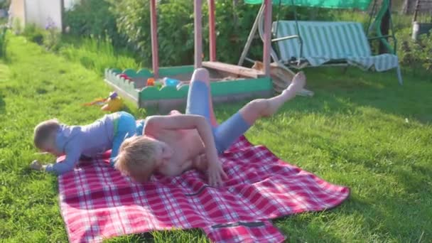 Zwei Kinder spielen an einem heißen Sommertag auf dem Rasen. Kinder lachen, sie rennen und fallen auf den Rasen. Outdoor-Unterhaltung. Glückliche Kindheit — Stockvideo