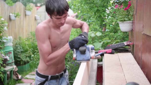 Man-Builder, trabajando en un banco de trabajo con herramientas eléctricas. Construcción de objetos de madera. Procesamiento de tablas de madera con una herramienta — Vídeo de stock