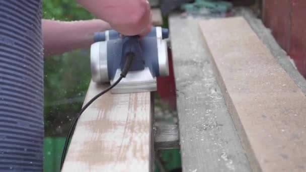 Bearbetning av brädor med ett verktyg. Mannen-Builder, arbetar på en arbetsbänk med elverktyg. Byggandet av föremål av trä. — Stockvideo