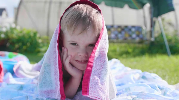 Un ragazzino sdraiato sul prato in una calda giornata estiva. Il bambino è divertente e attivo per trascorrere il tempo libero — Foto Stock