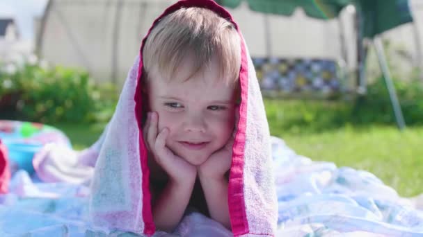 Ein kleiner Junge liegt und spielt an einem heißen Sommertag auf dem Rasen. das Kind ist lustig und aktiv in seiner Freizeit — Stockvideo