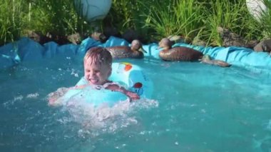 Çocuk küçük bir havuzda yüzüyor. Çocuk serin su sıcak yaz gününde sahiptir. Mutlu çocukluk. Çiçekler ve çim havuzun etrafında büyümek