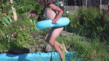 Küçük bir kız küçük bir su birikintisi içine atlamak su sıçramasına atlar. Çocuk serin su sıcak yaz gününde sahiptir. Mutlu çocukluk. Çiçekler ve çim havuzun etrafında büyümek