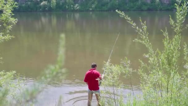 Fiskare med ett fiskespö ligger vid floden Bank. Vackra sommarlandskap. Friluftsliv och rekreation. Hobby — Stockvideo