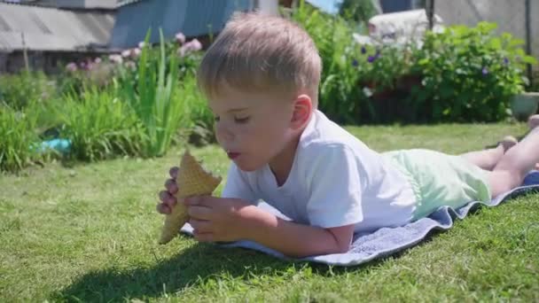 Un petit garçon allongé sur la pelouse et heureux de manger de la glace. Journée d'été chaude, dessert sucré froid 