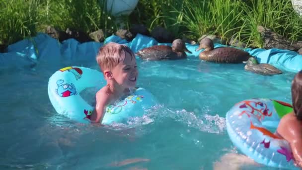 Zwei kleine Kinder schwimmen in einem kleinen Teich. Bruder und Schwester lachen und spritzen Wasser. Kinder schwimmen an einem heißen Sommertag. Glückliche Kindheit — Stockvideo