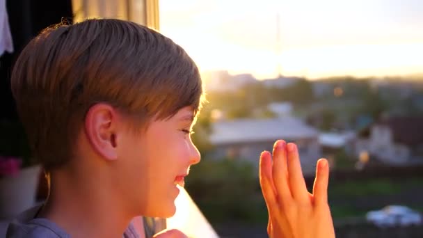 Un joven parado junto a la ventana por la mañana. Los primeros rayos del sol iluminan la habitación. El tipo agita la mano, da la bienvenida al comienzo del día — Vídeo de stock