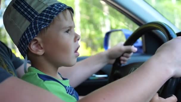 少年は、車に乗る。Hes は父親の腕に座っていると、ホイールを保持します。国の道路 — ストック動画