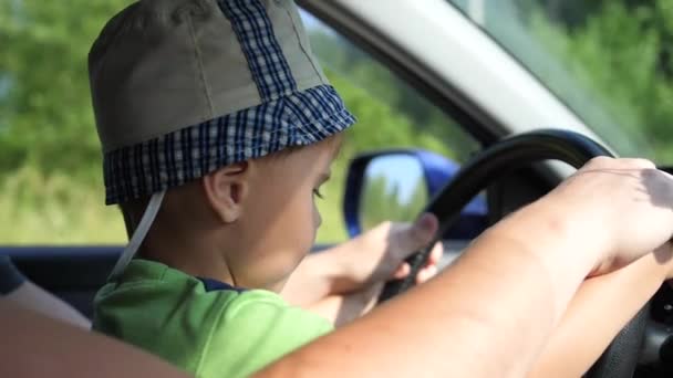 O rapaz entra no carro. Ele está sentado nos braços dos pais e segurando a roda. Estrada rural — Vídeo de Stock