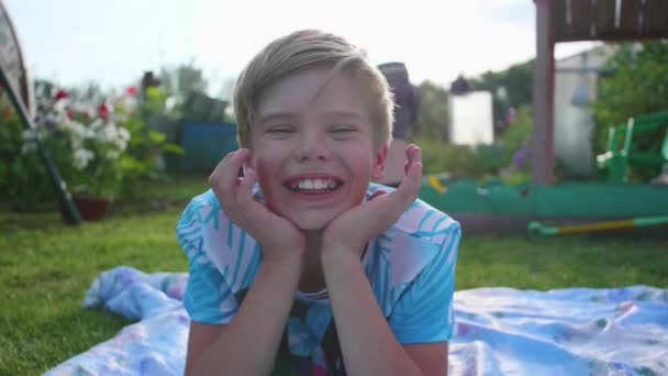 Il est allongé sur la pelouse par une chaude journée d'été. L'enfant est amusant et actif pour passer son temps libre — Video