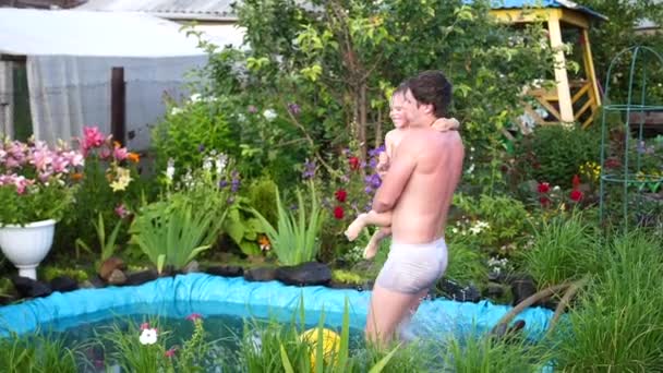 Rodinné mladý otec a jeho dítě plavat v malé jezírko v horkém letním dni. Chlapce skoky do vody, vytvoří tryskající vody. Zahrada, květiny a rostliny kolem jezera. Šťastné dětství — Stock video