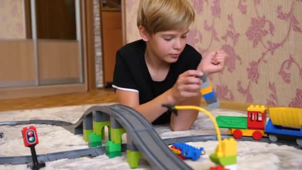 El niño juega con el ferrocarril de los niños.Un adolescente en la sala de juegos, jugando con un conjunto de construcción, objeto de colección hecho de pequeños ladrillos y piezas . — Vídeos de Stock