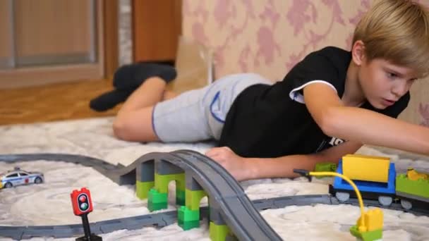 Barnet leker med barnens järnvägen. En tonåring i lekrummet, leker med ett set, samling objekt gjorda av små klossar och delar. — Stockvideo