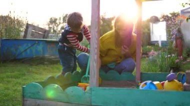 kum havuzunda oynayan bir çocuk ile genç bir anne. Yaz günü, Güneş ışınları parkta