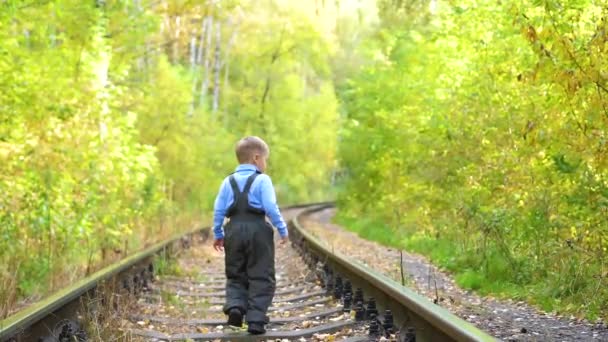 鉄道の線路の上を歩く孤独な少年。危険なゲームとエンターテイメント。秋の日 — ストック動画