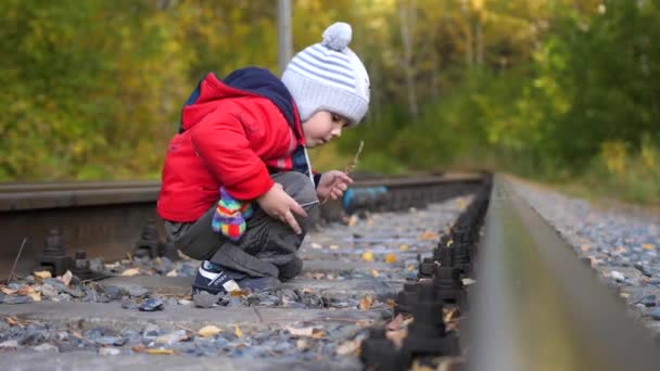 Ensam pojke spelar på järnvägsspåren. Farligt spel och underhållning. Varm höstdag. — Stockvideo