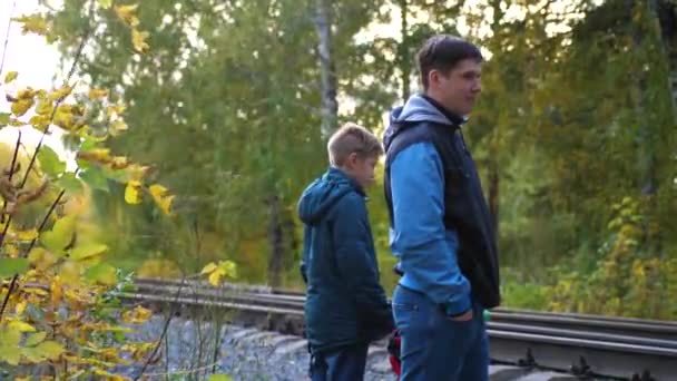 Spoorwegovergang. De familie staat in de buurt van de spoorlijn en kijkt naar de passerende locomotief. Herfst Park, een pittoreske plaats — Stockvideo