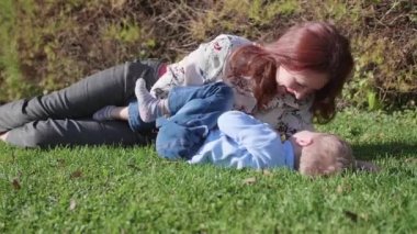 Mutlu bir aile çimenlerin üstünde dinlenme. Şefkat ve sevgi ile anne çocuğunu evlat güler sarılmak. Mutlu çocukluk