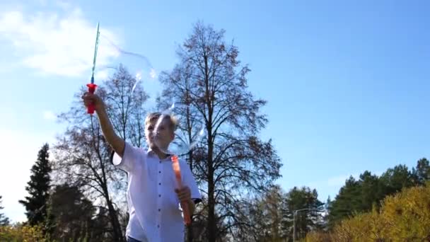 En ung kille i parken gör stora såpbubblor. Semester och underhållning utomhus — Stockvideo