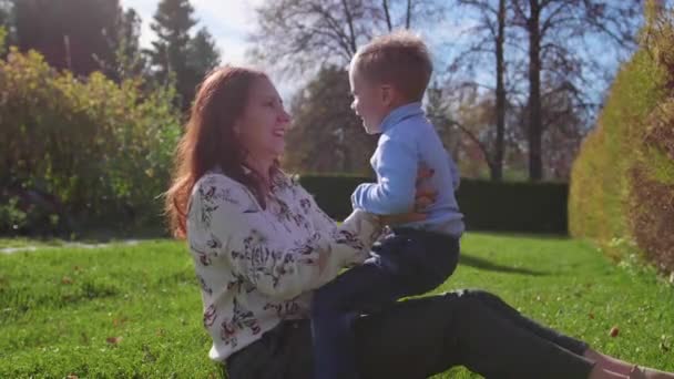 Feliz familia descansando en el césped. Madre con ternura y amor juega con su hijo, el hijo se ríe, él se divierte. Feliz infancia. — Vídeo de stock