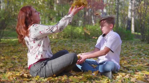 妈妈和儿子在秋季公园玩。他们扔黄叶。愉快的户外消遣 — 图库视频影像